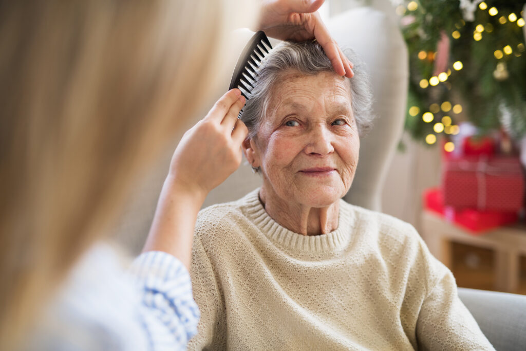 A person is providing family caregiving to their elderly relative by combing her hair