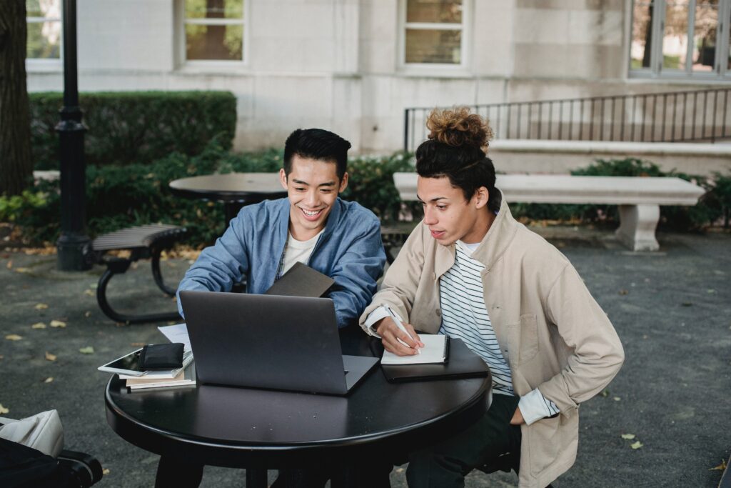 Two young men are looking at their laptop, discussing family caregiver options that will work for their loved one